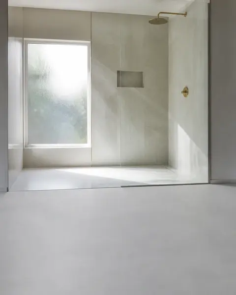 Bodengleiche Dusche mit Glaswand und hellen großformatigen Fliesen, Tageslicht durch ein mattiertes Fenster